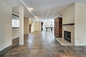 A spacious and well-lit basement featuring slate flooring and a fireplace.